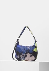 Torebka z kwiatowym wzorem w kolorach niebieskim, czarnym i zielonym, w kształcie półksiężyca, z wyściełaną rączką, prezentowana na białym postumencie na białym tle.