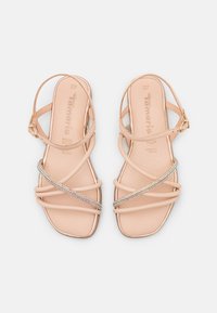 Nude-näyttävät remmisandaalit, joissa on tasainen pohja. Kenkien päällä on useita hihnoja, ja keskijalan alueella on kimaltava strassikoriste. Koko 37 on merkitty.