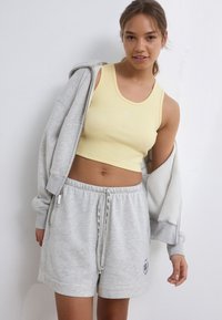 Sweat-shirt gris avec un crop top côtelé jaune et un short gris, doté d'une taille à cordon de serrage et d'un détail logo sur le short.