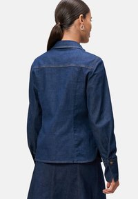Ciemnoniebieska kurtka dżinsowa z długimi rękawami, mankietami na guziki i klasycznym kołnierzykiem. Posiada kontrastowe przeszycia i dopasowany fason.