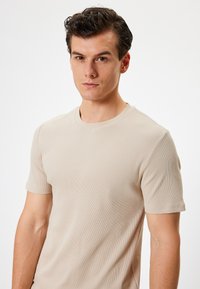 Kortærmet beige ribbet t-shirt med rund hals. Stoffet har en glat tekstur og sidder tæt til kroppen med subtile syningsdetaljer.
