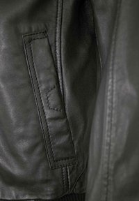 Nahaufnahme einer schwarzen Lederjacke, die die glatte Textur zeigt, eine Vordertasche mit sichtbaren Nähten und gerippte Bündchen am Saum.