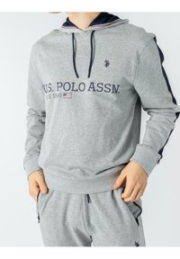 Šedá mikina s námořnickou kapucí, obsahuje text "U.S. POLO ASSN." a vyšívané logo. Zahrnuje žebrovaný pás a manžety.