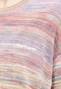 Nahaufnahme eines mehrfarbig gestreiften Strickpullovers mit "carhartt" in Weiß auf der Brust gestickt.