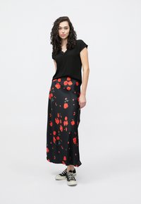 Sort blomstrete skjørt med røde roser, silkelignende tekstur og et luftig design, kombinert med en svart topp med korte ermer og svarte joggesko.