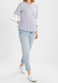 Top peplum a righe blu e bianche con maniche a campana, con dettagli in pizzo. Abbinato a jeans blu chiaro e sneaker bianche.