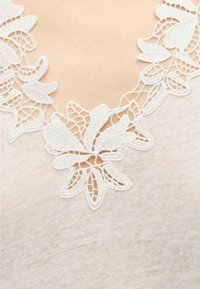 Gros plan d'un tissu beige avec une bordure en dentelle florale blanche le long d'un décolleté en V.