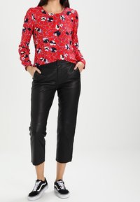 Top lungo a maniche corte rosso con dettagli in bianco e nero, abbinato a pantaloni in pelle neri alla caviglia e sneakers nere con suola bianca.