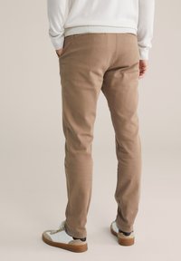 Hnědé bavlněné kalhoty slim fit, se bočními kapsami a hladkým povrchem, doplněné bílými a šedými teniskami pro ležérní vzhled.