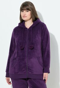 Haut de hoodie zippé en polaire violet avec capuche, poches avant et cordons avec pompons. Texture douce avec des poignets et un ourlet côtelés.