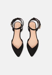 Chaussures plates en daim noir à bout pointu avec brides de cheville et boucles ton or, vues de dessus sur fond blanc.