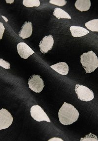 Tessuto nero con pois bianchi, caratterizzato da un aspetto tessuto e testurizzato. I pois variano in dimensione e sono distribuiti in modo irregolare su tutto il materiale.