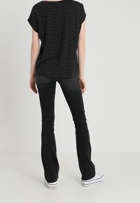 Black polka dot top with a loose fit, short sleeves, and a rounded hem, paired with flared black jeans and white sneakers.