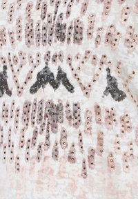 Textil s vzory v odstínech růžové, šedé a bílé, zdobený kovovými zlatými hřebíky uspořádanými do různých tvarů a designů.