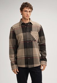 Brązowa i czarna flanelowa koszula w kratę z zapięciem na guziki, spiczastym kołnierzem i kieszenią. Charakteryzuje się czerwonymi liniami i teksturowanym wykończeniem materiału.