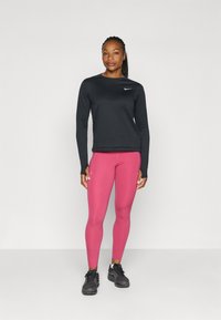 Sort langærmet træningstop, pink leggings og sorte sneakers. Bemærkelsesværdige detaljer inkluderer et hvidt Nike-logo på toppen og en tætsiddende design.