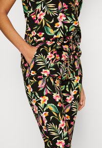 Floral, black jumpsuit with vibrant pink, yellow, and green patterns. Features a cinched waist and side pockets for added practicality.