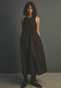 Zwarte, mouwloze jurk met een aansluitend lijfje en een uitlopende rok. Gemaakt van een zachte stof, met zijzakken en een minimalistisch design.