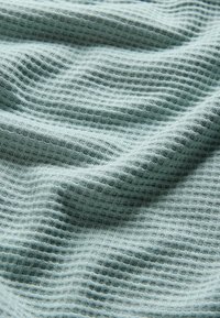 Puha világoskék gofréfonal anyag, finom hajtásokkal és texturált rácsmintával, közelről látható.