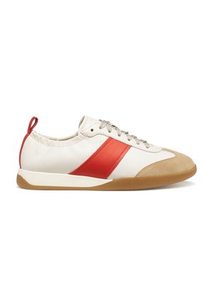 Zapatilla blanca de corte bajo con franja lateral roja, puntera de ante color beige, cordones beige, lazo rojo en el talón y suela de goma marrón, mostrada de perfil.