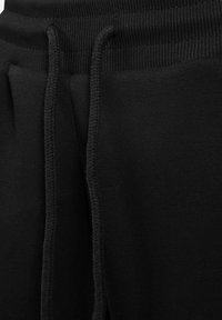 Lähikuva mustista treenihousuista, jossa on ribbed-elastinen vyötärö ja kankaiset nyörit roikkumassa etuosa keskipisteestä.