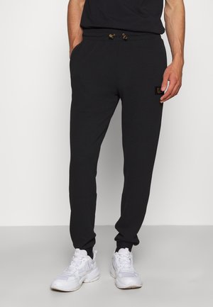 Black jogger pants with a textured fabric, elastic waistband, drawstring closure, and side pockets; features a small logo patch on the thigh.