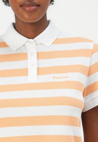 Polo shirt in oranje en witte strepen, van katoenmateriaal. Bevat een kraag, drie knopen en geborduurd "Barbour" op de borst.