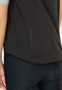 Schwarzes Sportshirt mit strukturierter Oberfläche, das das Wort "ENDURANCE" am Saum eingestickt hat. Dazu dunkelblaue Leggings.