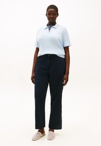 Ανοιχτό μπλε πλεκτό πόλο πουκάμισο, ναυτικό μπλε παντελόνι και λευκά υφαντά παπούτσια τύπου slip-on. Το σύνολο έχει άνετη εφαρμογή και διακριτικό ριγωτό γιακά.