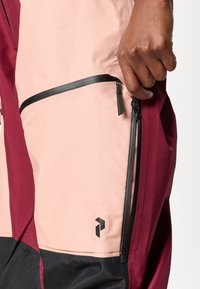 Bordové a rúžové ľahké nohavice s čiernymi akcentmi. Obsahujú zipsové vrecká a logo. Hladká textúra. Dôraz na praktickosť a štýl.