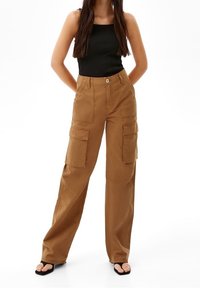 Cargo-byxor i en ljusbrun material, med en lös passform, vida ben och flera sidofickor. Kombinerat med en svart ribbad linne.