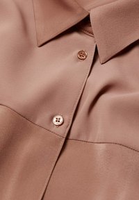 Różowa satynowa bluzka z kołnierzykiem, z zapięciem na guziki z przodu i gładką teksturą. W szczegółach wyróżniają się okrągłe, błyszczące guziki.