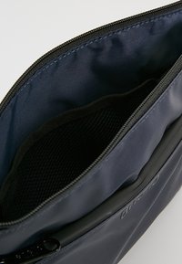 Astuccio con zip di colore blu navy realizzato in nylon con un'esterno testurizzato. L'interno presenta una tasca in rete per l'organizzazione. Design semplice e funzionale.
