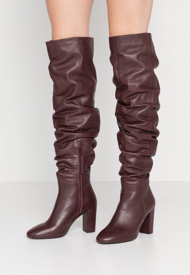 Botas de cuero burdeos por encima de la rodilla con diseño holgado, tacones cuadrados, cremallera lateral y acabado suave.