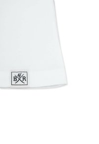 Valkoinen puuvillainen T-paita, jossa on pehmeä tekstuuri ja lyhyet hihat. Siinä on suorakulmainen musta etiketti, jossa on ristikkäin kirjletterit "B" ja "R".
