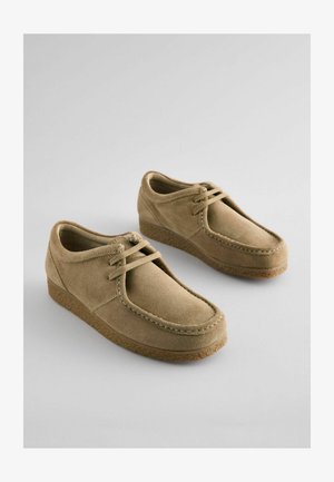 Beige Wildlederschuhe mit runder Zehenpartie, Schnürung vorne und niedriger Gummisohle. Verfügt über eine genähte Verzierung entlang der Kante.