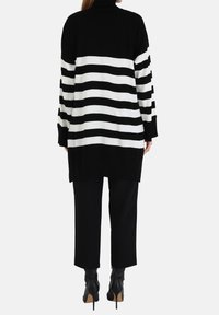 Pull à rayures noires et blanches avec un col montant, coupe oversize et manches longues, associé à un pantalon court noir et des bottines.