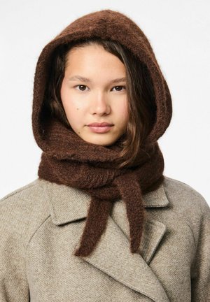 Smeđi šal od vune s kapuljačom, s mekanom, pahuljastom teksturom, vezan naprijed. Nosite preko svijetlosivog, teksturiranog kaputa.