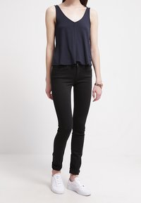 Top sin mangas azul marino con escote en V, combinado con jeans ajustados negros y zapatillas blancas. Tela suave y diseño casual.