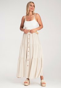 Beiges, gestuftes Maxikleid mit Knopfdetails, taillierter Taille und geflochtenem Gürtel; kombiniert mit klobigen, geflochtenen Sandalen.