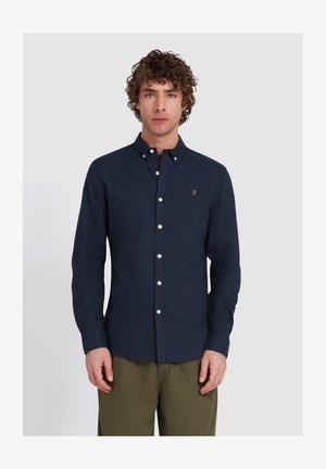 Marineblaue Knopfleiste aus Baumwollstoff, mit einem Logo auf der Brust, weißen Knöpfen und langen Ärmeln.