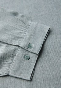 Collo di camicia azzurro chiaro con dettaglio arricciato, caratterizzato da due bottoni rotondi abbinati e un tessuto morbido e textured.