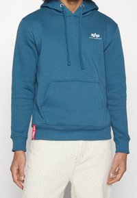 Felpa con cappuccio blu in cotone, con tasca a marsupio, cappuccio con coulisse e piccolo logo bianco sul petto. Dettaglio con etichetta rossa sull'orlo.