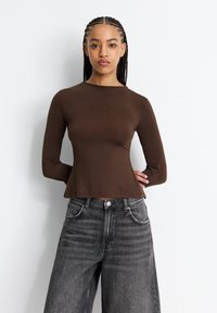 Maglione marrone a maniche lunghe con scollatura rotonda, silhouette aderente e orlo svasato. Abbinato a jeans scuri a vita alta e gamba larga.