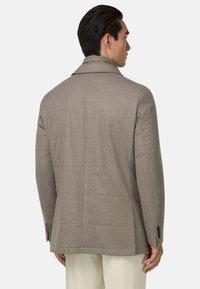 Giacca marrone su misura con un design strutturato, texture liscia e cuciture quadrate, dotata di colletto a scollatura e polsini con bottoni.