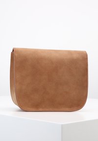 Bolso cruzado de ante marrón con una textura suave, bordes redondeados y un cierre de solapa. Diseño minimalista sin herrajes visibles.