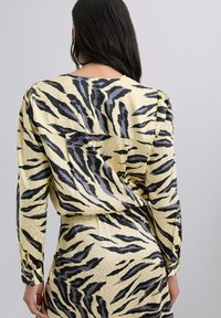 Vestido de manga larga en tejido de satén con un fondo amarillo que presenta un patrón de rayas de tigre en negro y gris. Corte ligeramente holgado con un pliegue en la parte posterior.