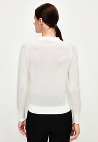 Witte trui met lange mouwen van een zachte, lichte stof, met een gebandeerde onderrand en manchetten. Strak, minimalistisch ontwerp zonder versieringen.