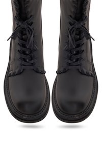Paire de bottes noires en cuir à lacets avec bouts arrondis et semelles épaisses, vues de dessus sur un fond blanc.