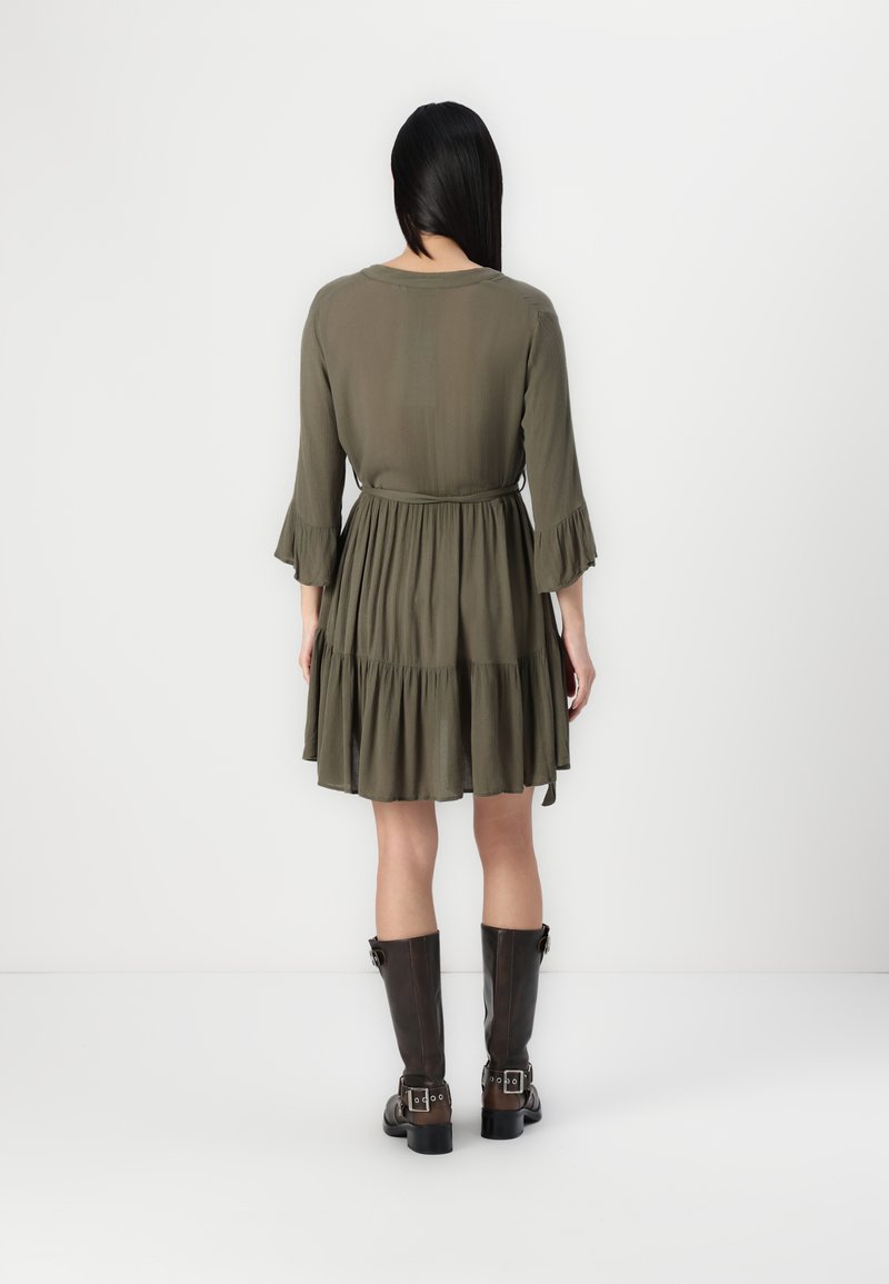 Robes vert olive, longueur genou, à boutons avec des manches évasées et une taille cintrée, assorties à des bottes en cuir marron jusqu'aux genoux.